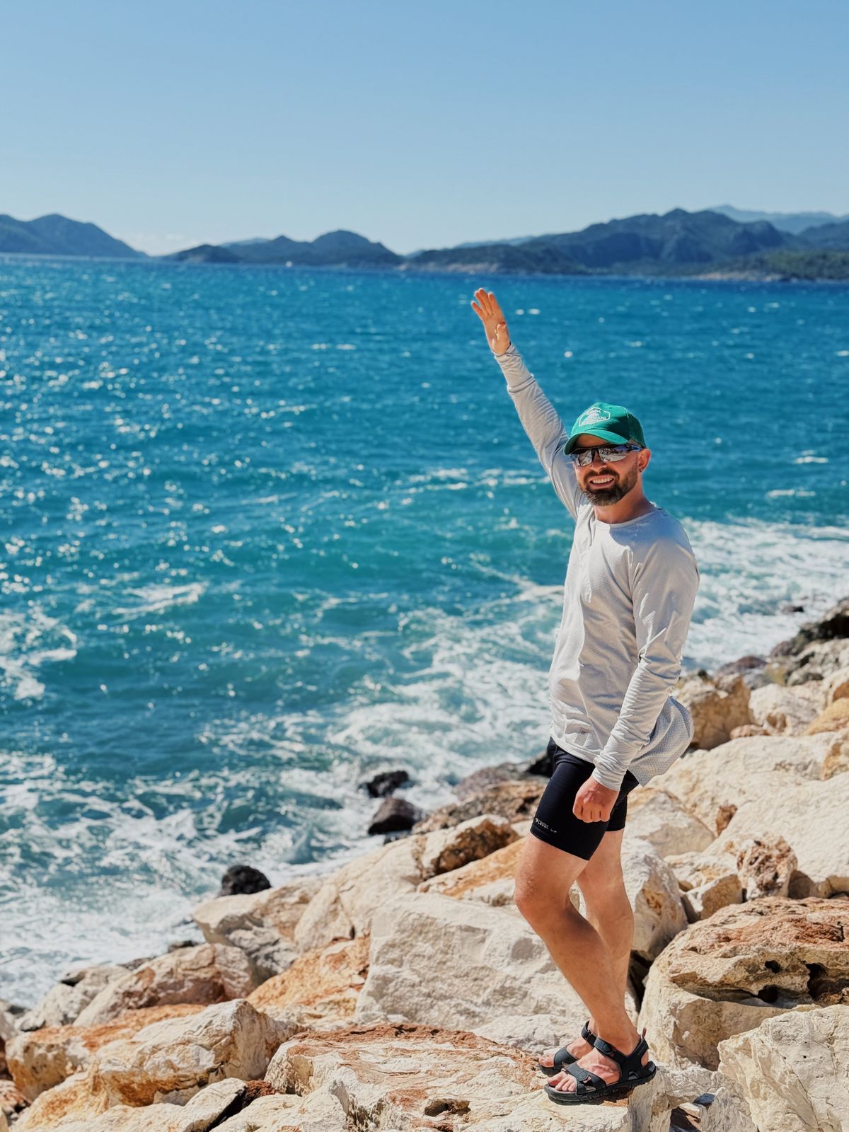 A man wearing a long-sleeved top, shorts and sandals by the coast.