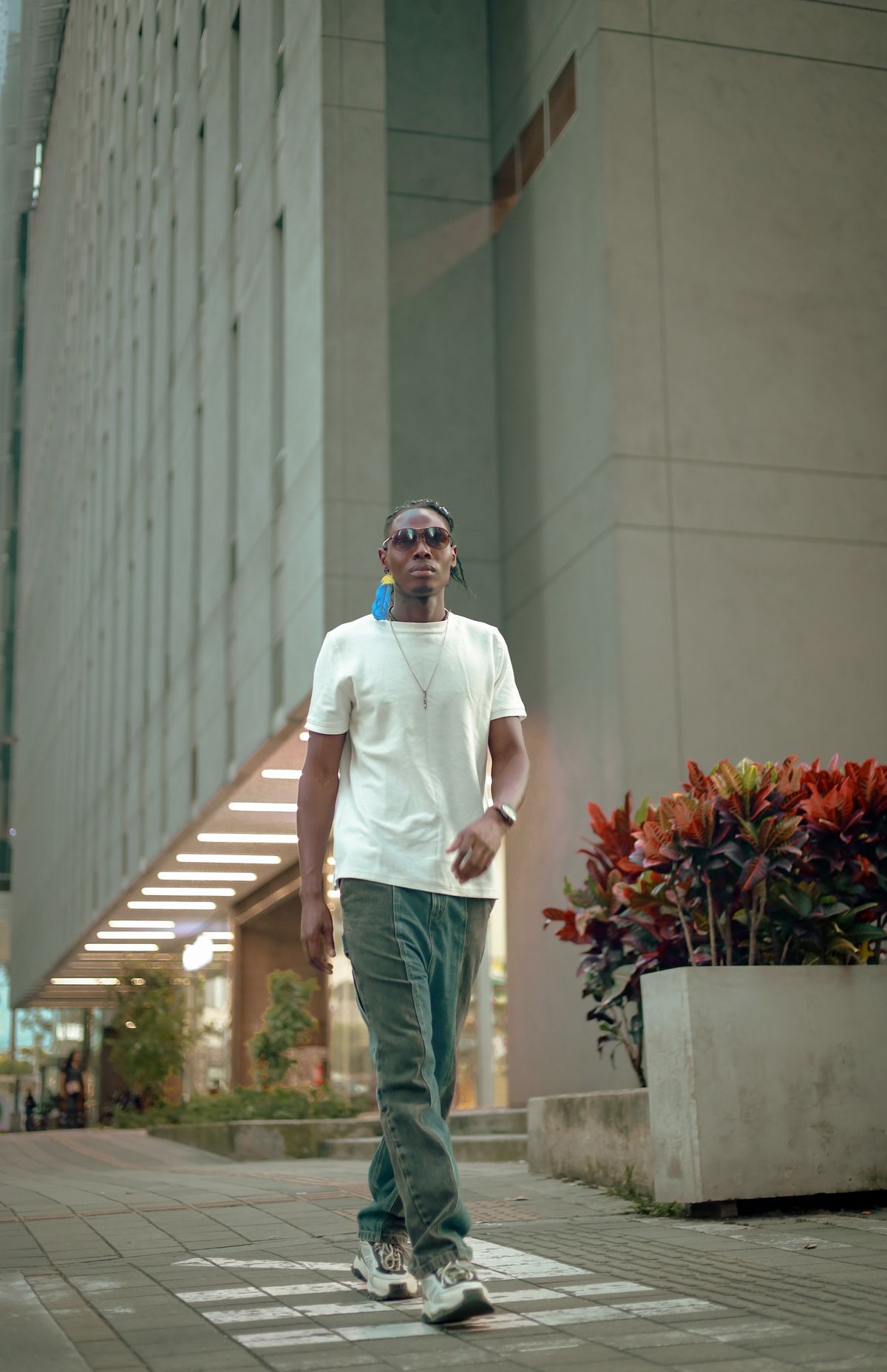A man walking in trainers, green trousers and a light T-shirt.
