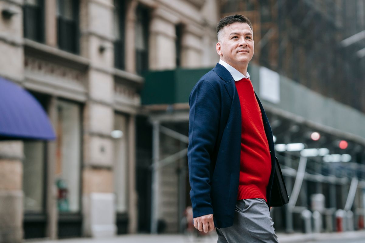 A bright red jumper adds colour to a navy jacket and grey trousers.