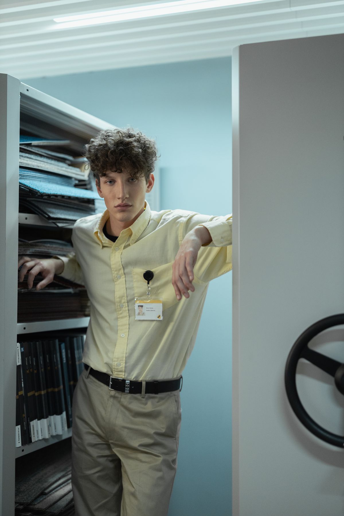 A tucked pale-yellow shirt and stone trousers in an office.