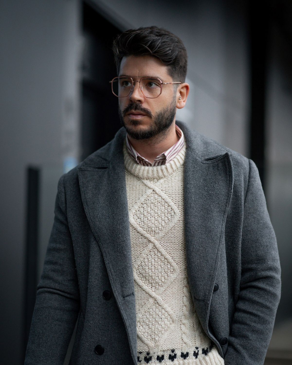 A grey overcoat layered over a patterned cream knit and shirt.