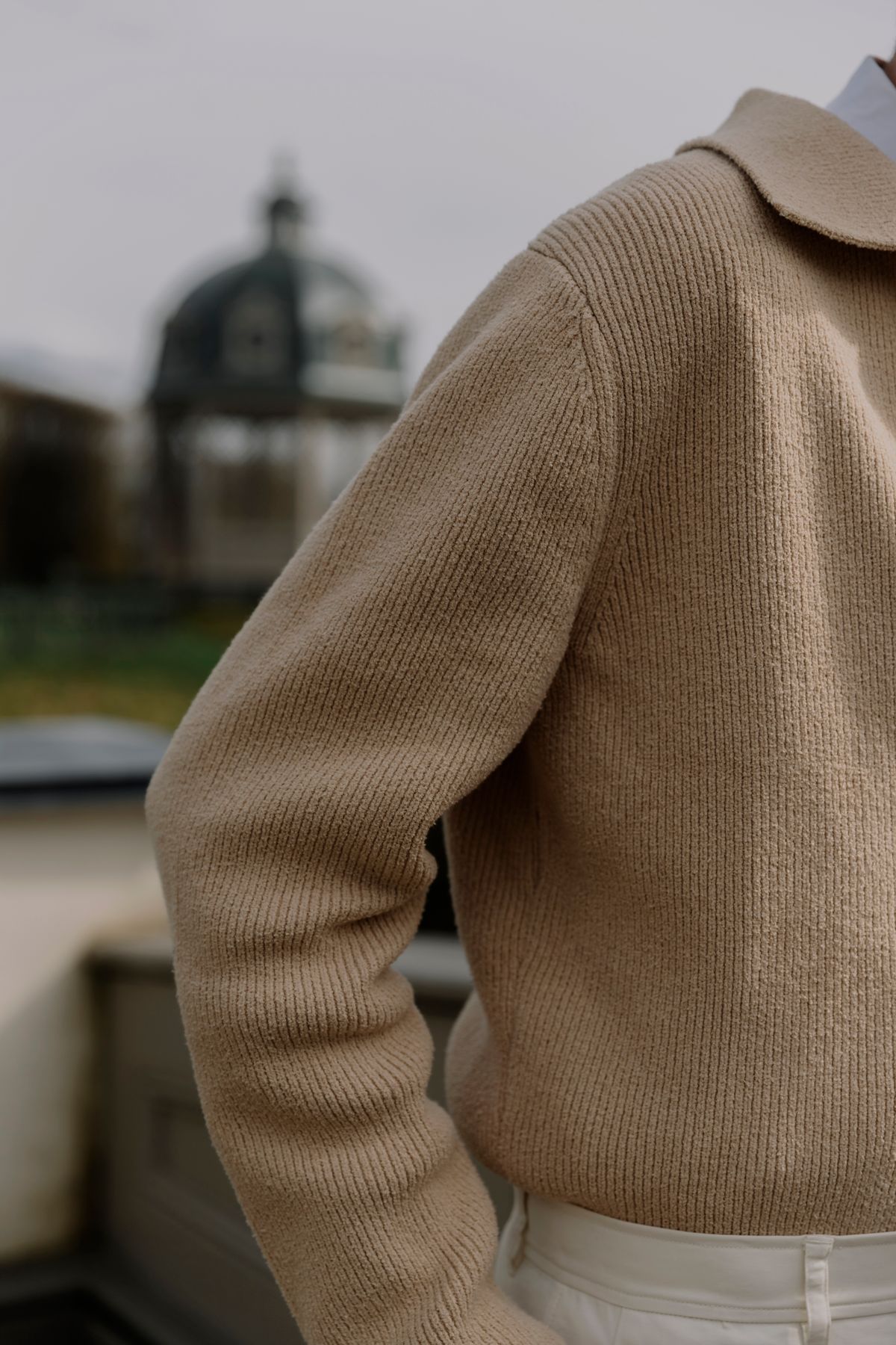 A brown knitted collared top tucked into cream trousers.