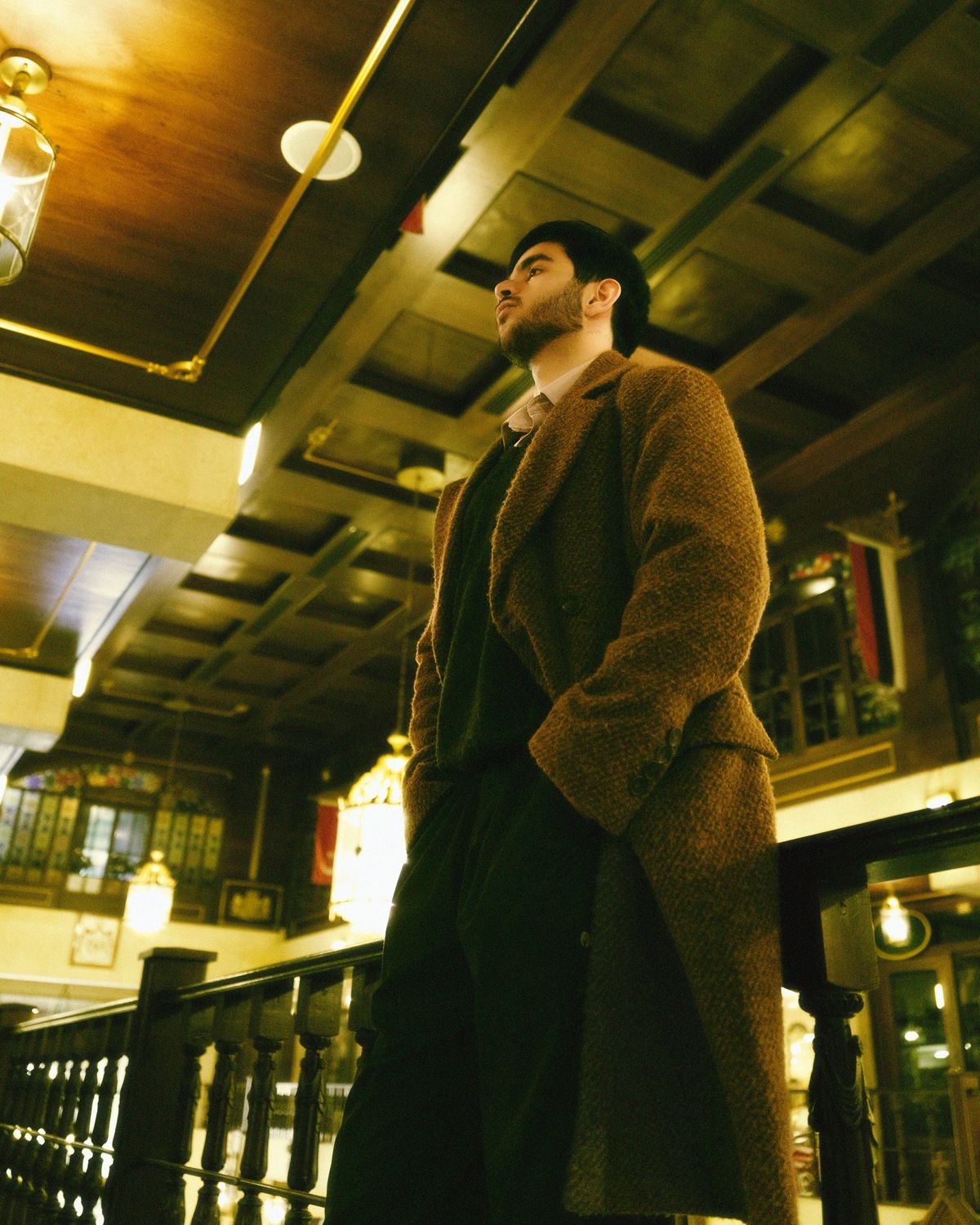 A long brown textured overcoat worn over dark knitwear.