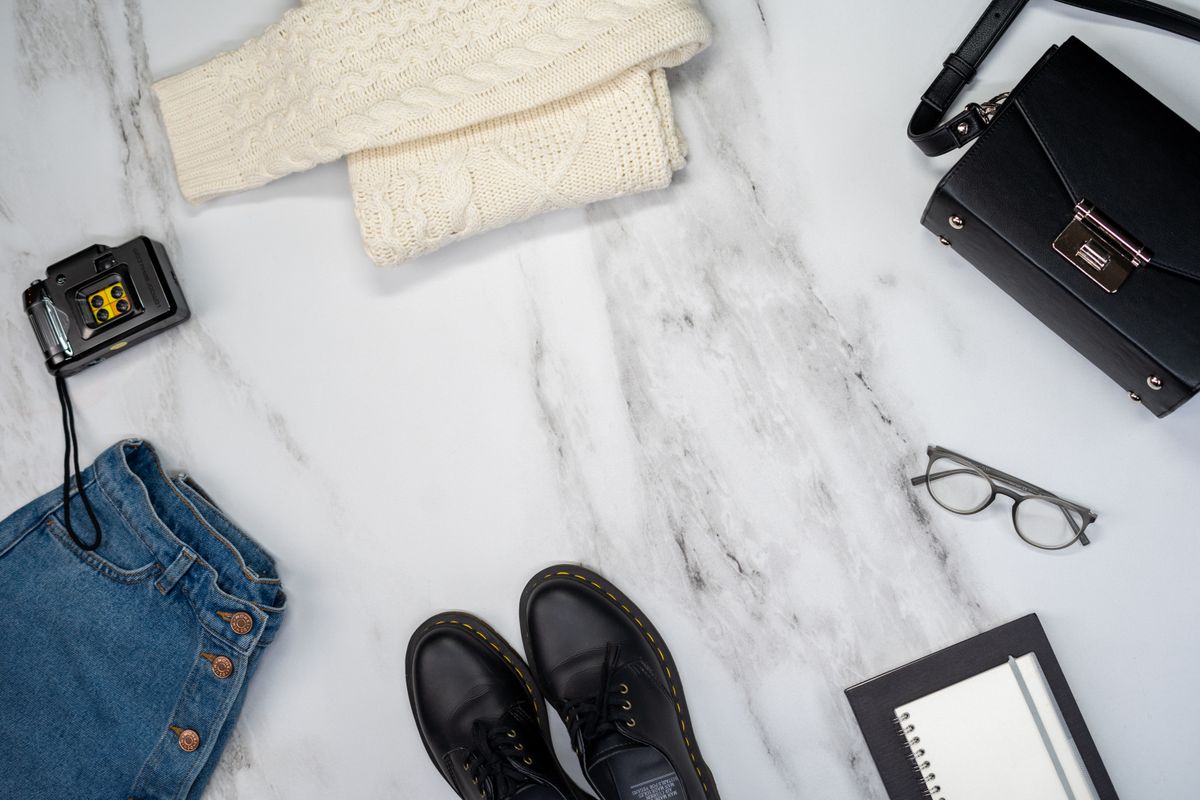 A flat lay of jeans, a cream knit, black loafer and accessories.