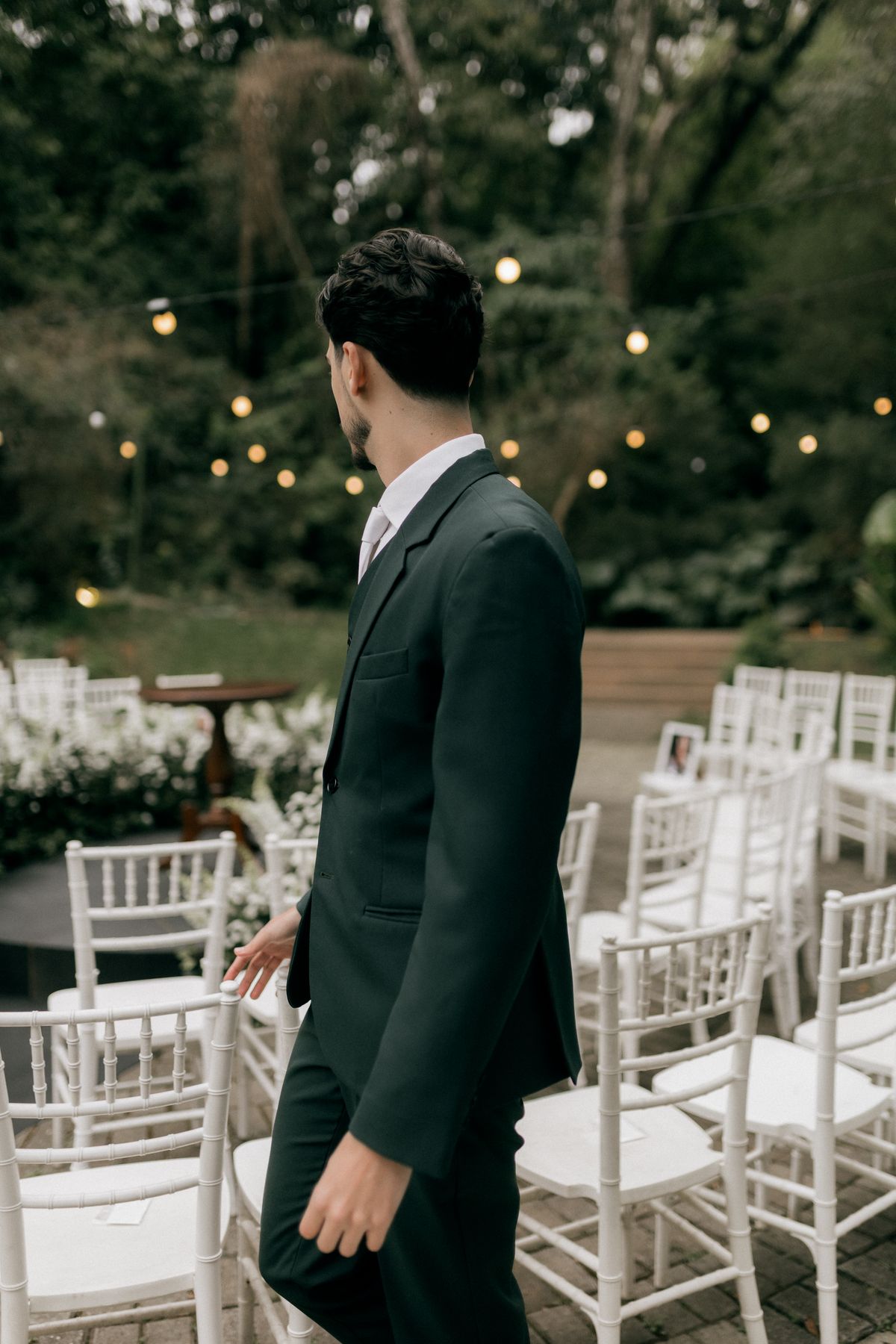 A man in a dark suit beside chairs at an outdoor wedding venue.