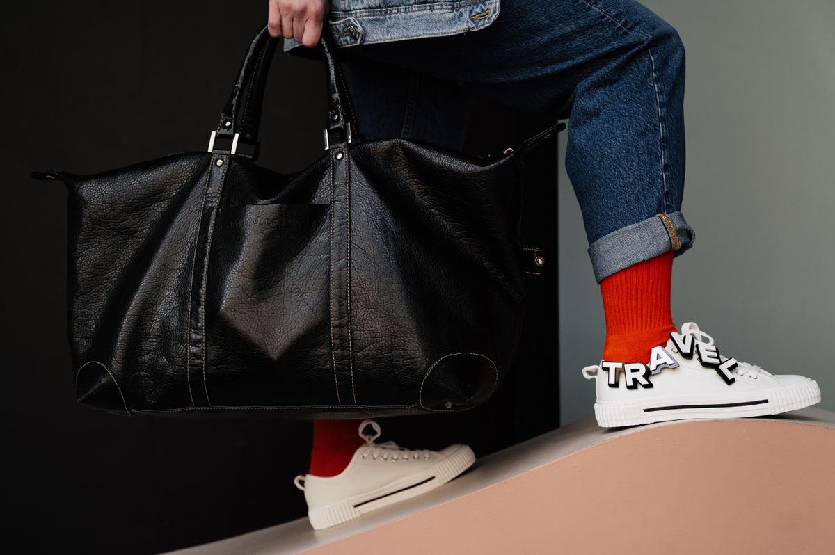 A black leather holdall carried beside jeans and trainers.