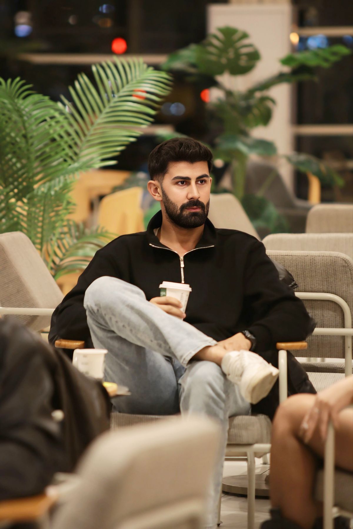 A man wearing a dark overshirt and pale jeans in a cafe.